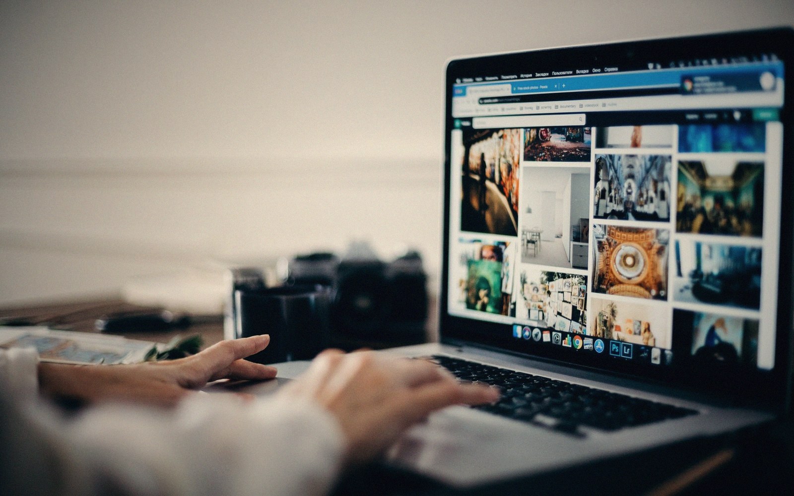 Hands typing on a laptop displaying a grid of photo thumbnails in a browser window