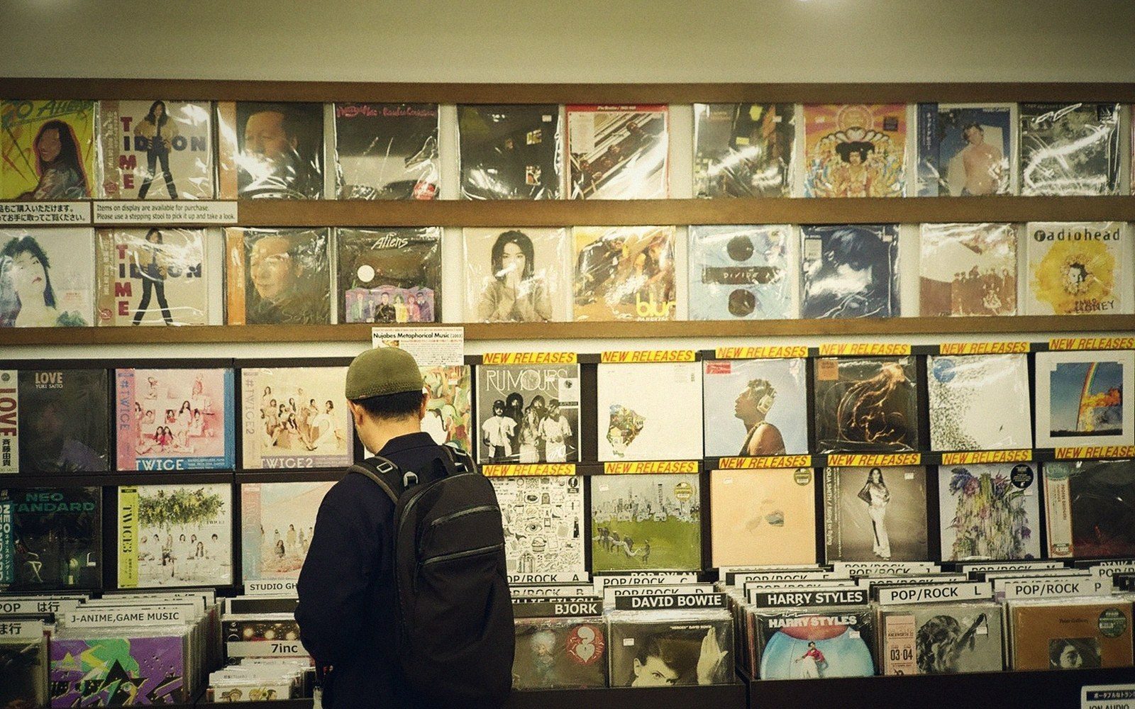 A shopper wearing a backpack browses vinyl records displayed on shelves in a record store