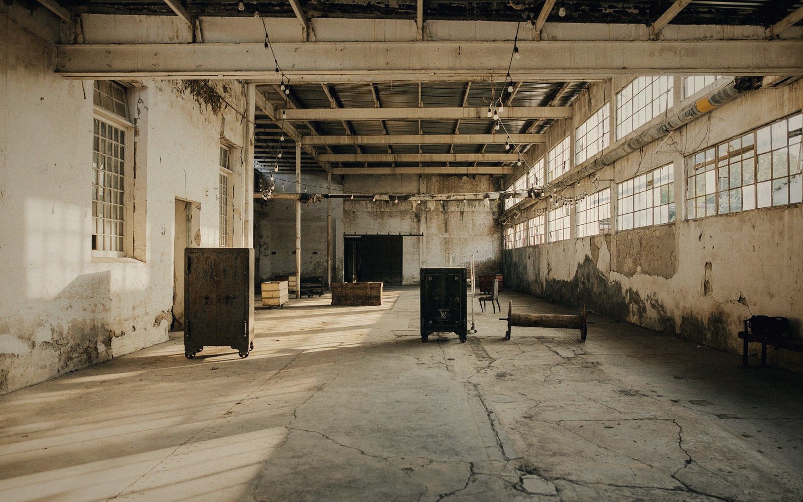 Empty industrial warehouse with rows of windows, exposed beams, and scattered old cabinets