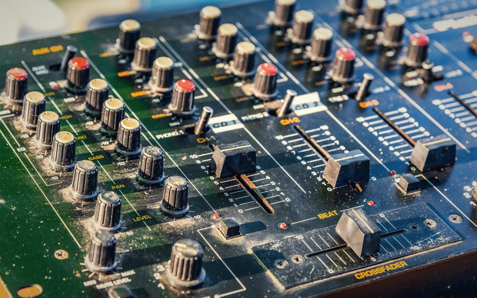 A DJ mixer under amber light, faders and EQ knobs visible on a worn table